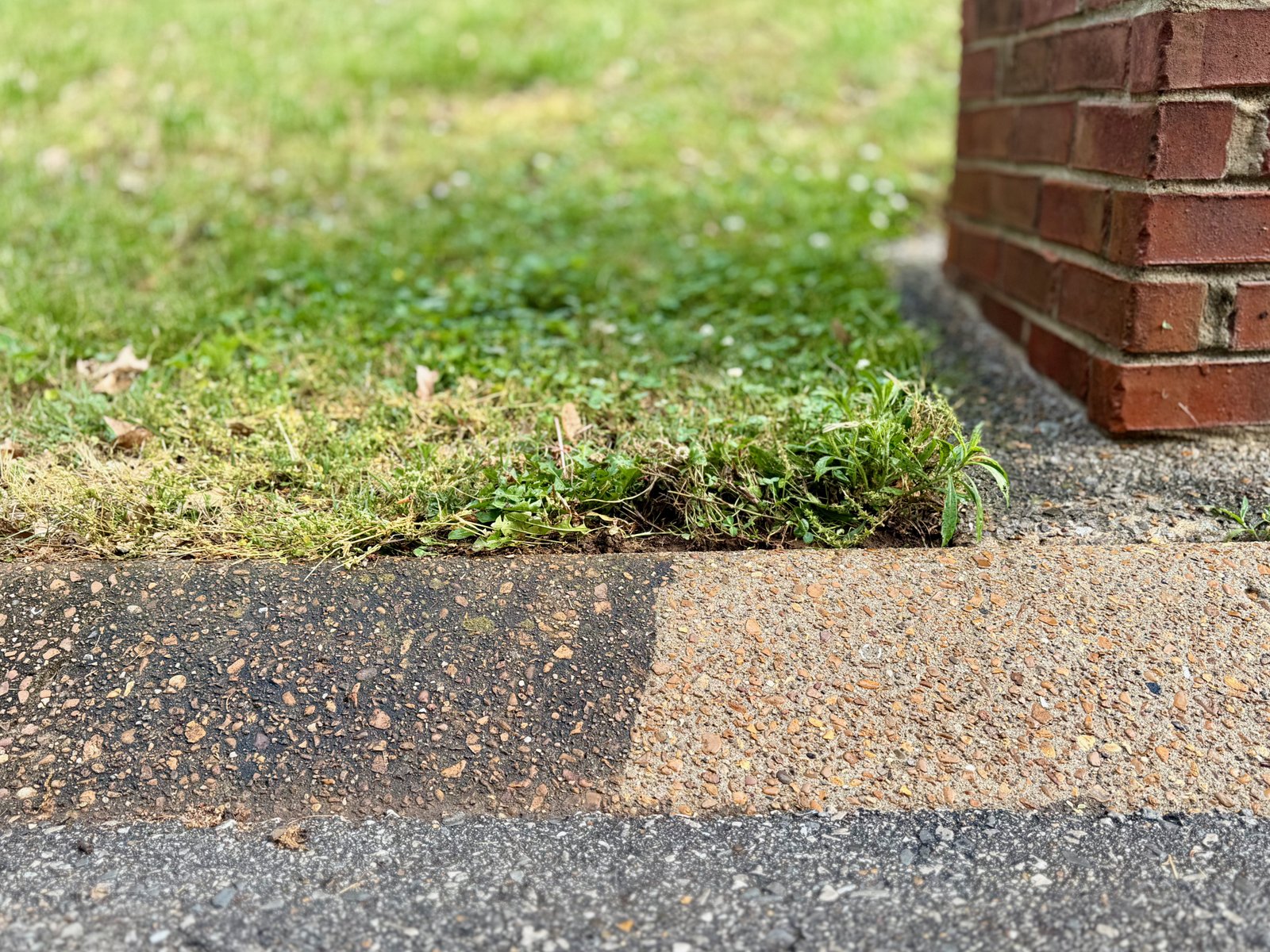 Side-by-side of a residential curb. The left half is dark with years of road grime; the right is the original concrete and pebble surface.